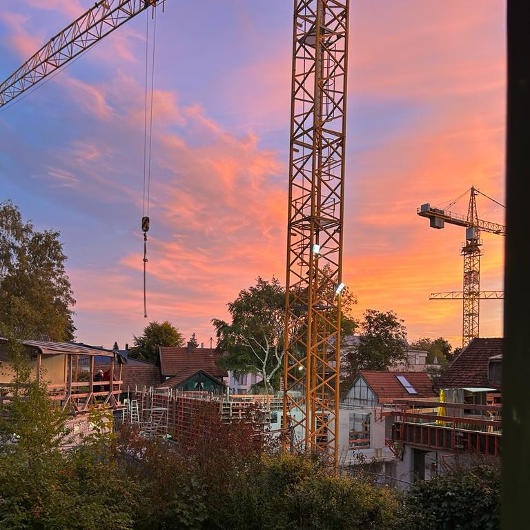Baustelle mit Turmdrehkranen in einem Münchner Wohnviertel bei Abendrot